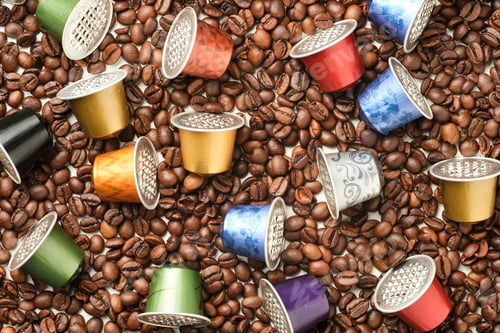 Preview: image from above of colored coffee capsules on surface full of coffee beans