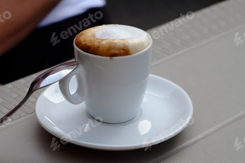 Preview: Steaming cup of cappuccino standing on a saucer with spoon resting on the rim
