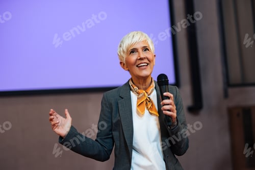 Preview: Senior businesswoman giving a speech in the conference hall, elegantly dressed.