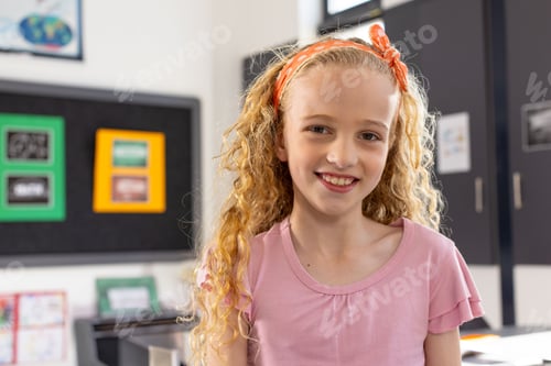 Preview: girl child standing and smiling in bright classroom, with bulletin board, world map and desk books