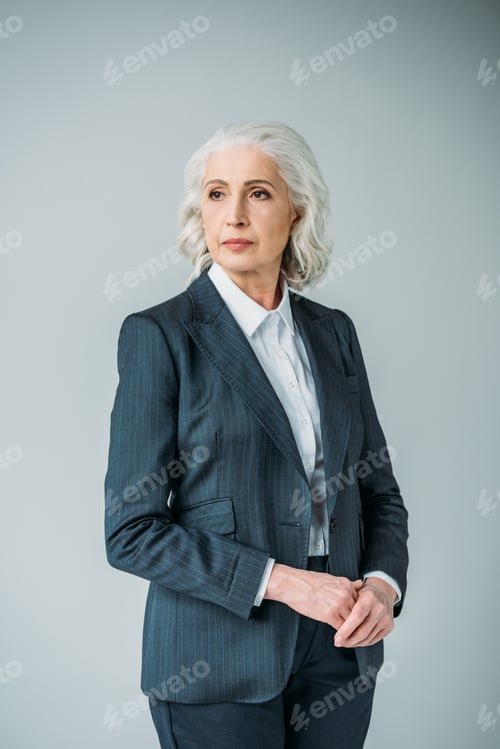 Preview: pensive senior businesswoman in suit looking aside isolated on grey