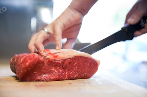 Preview: Close up of butchers hands slicing raw steak on butchers block
