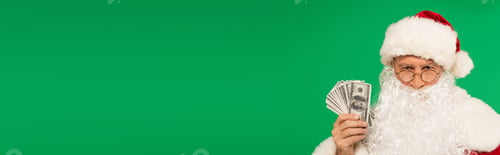 Preview: Santa claus looking at camera and holding cash isolated on green, banner