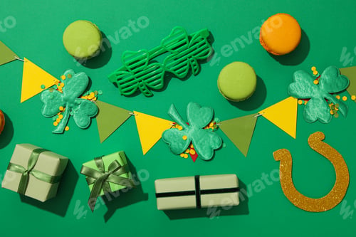 Preview: Clover leaves, paper flags, gift boxes and cookies on green background, top view