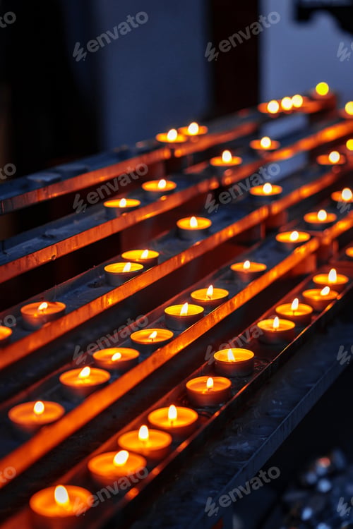 Preview: Candles lit on a metal rack in a dim space during evening hours