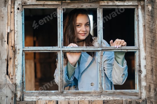 Preview: girl looks out the window from an old wooden house