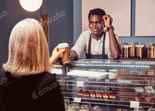 Preview: African American barista in uniform giving a cup of coffee to his client at the trendy coffee shop