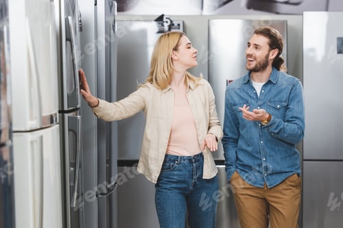 Preview: smiling boyfriend pointing with hand and girlfriend touching fridge in home appliance store