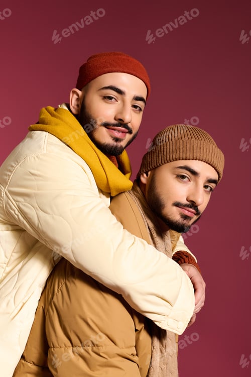 Preview: Stylish twins share a warm embrace in trendy winter fashion against a vibrant backdrop