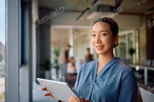 Preview: Smiling Korean female entrepreneur working on touchpad in the office and looking at camera.
