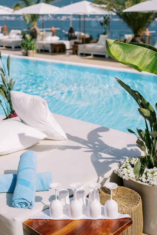 Preview: Row of glasses stands upside down on a table near a double sun lounger by the pool