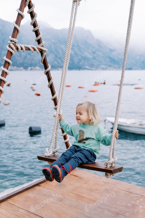 Preview: Little smiling girl swings on a swing on a pier by the sea