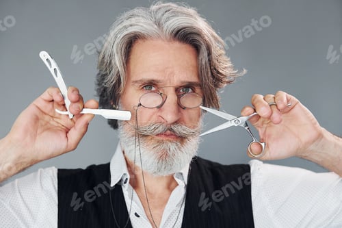 Preview: Against grey background. Stylish modern senior man with gray hair and beard is indoors