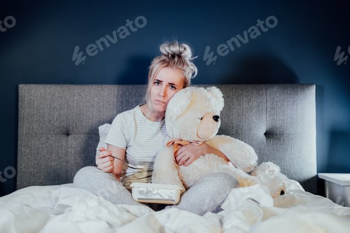 Preview: Heartbroken young woman huggying big teddy bear, eating ice cream from bucket while watching movie