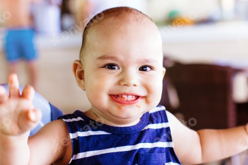 Preview: Happy little baby boy with dirty face in restaurant at hotel. Family vacation with children