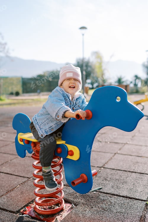 Preview: Little laughing girl swings on a swing-spring on the playground holding the handles