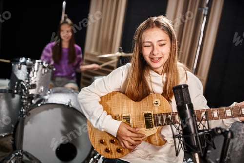 Visualização: concentre-se em uma linda adolescente tocando violão e cantando ao lado de sua amiga desfocada tocando bateria
