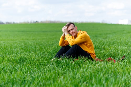 Preview: A young man sitting on green grass is thinking about the future. Handsome guy is relaxing