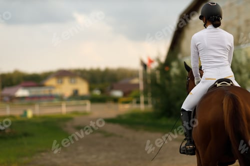 Preview: Woman rider jockey in helmet and white uniform preparing horse racing with copy space.