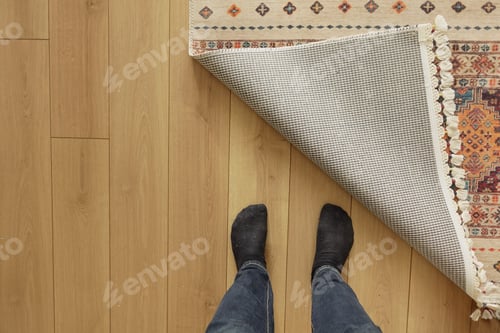 Preview: Feet standing on floor as a rug is pulled back in a home setting