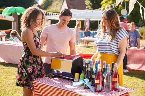 Preview: Couple At Tombola Stall At Busy Summer Garden Fete
