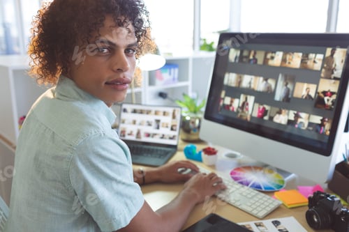 Preview: Handsome mixed race male graphic designer looking at camera while working on computer