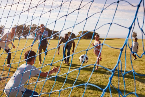 Preview: Two families playing football in park seen through goal net