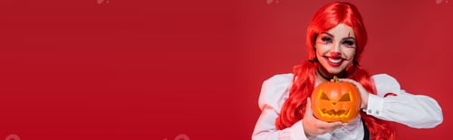 Preview: cheerful clown style woman with jack o lantern looking at camera isolated on red, banner