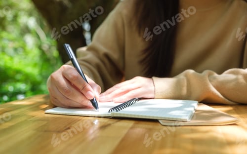 Preview: Closeup image of a woman writing on a notebook in the outdoors