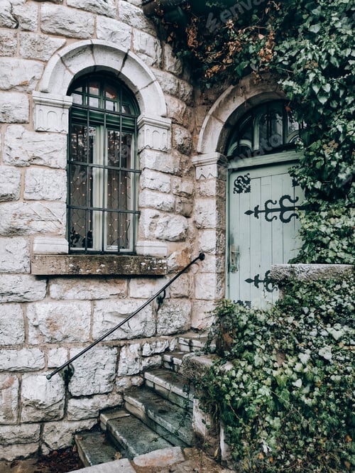Preview: Vertical shot of stairs to the door on an old stone wall house with greenery