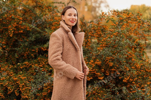 Preview: Smiling positive woman in a soft coat enjoys a day of beauty in nature
