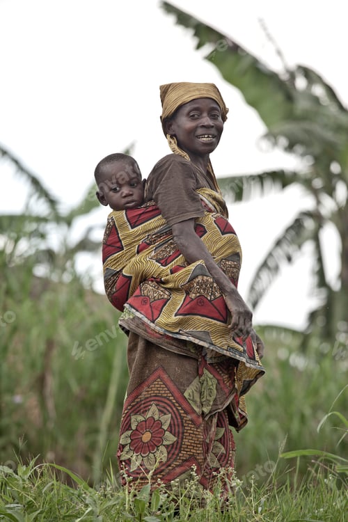 Preview: Mother carrying her child on her back amidst a lush green backdrop