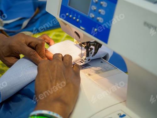 Preview: close up of adult black seamstress use sewing machine to skillfully sew a shirt with precision care