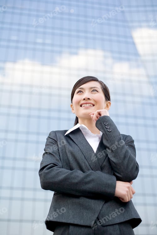 Preview: Young businesswoman standing in front of a tall building