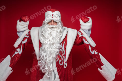 Preview: Serious senior male in xmas Santa Claus costume posing on red background celebrating new year