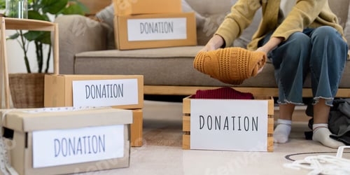 Preview: Woman placing warm knitted sweater into donation box, organizing clothes in a cozy living room