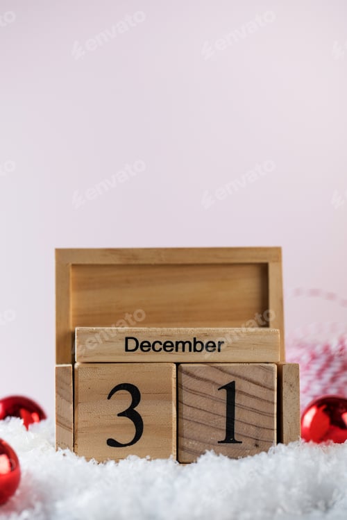 Preview: Composition of wooden block calendar with New Year eve date and small red balls in artificial snow.
