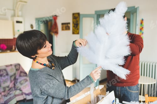 Preview: Young couple at home decorating xmas tree