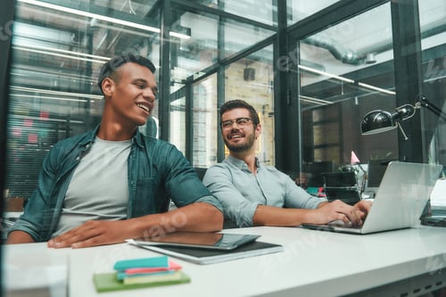 Preview: Positive atmosphere. Two young and handsome men talking with each other and smiling while working in