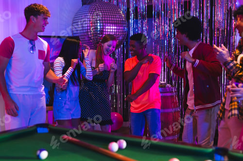 Preview: Teens dancing joyfully at party near pool table under disco ball lights