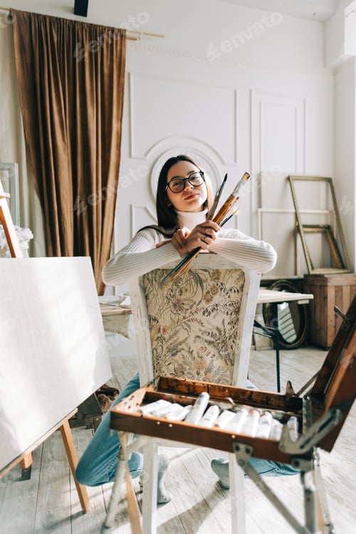 Preview: Woman Artist Smiling While Holding Paintbrushes in Studio
