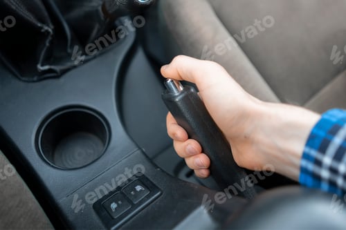 a close up cropped hand using the handbrake, driver sitting inside the car