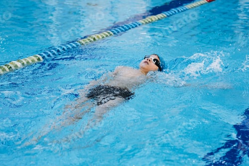 Preview: little caucasian boy wearing goggles swimming backstroke in a pool
