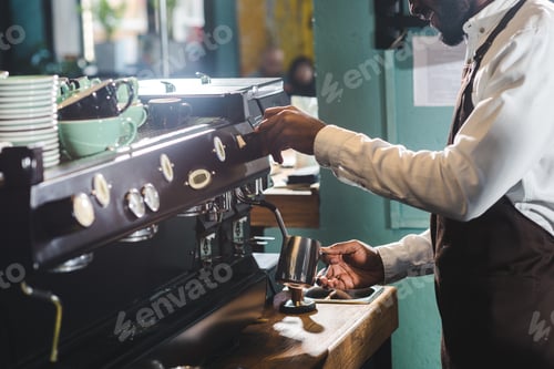 Preview: cropped shot of smiling african american barista making cappuccino at coffee machine