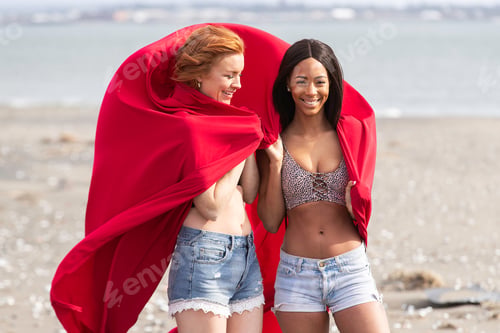 Preview: Two women playing with colorful fabric at the ocean beach