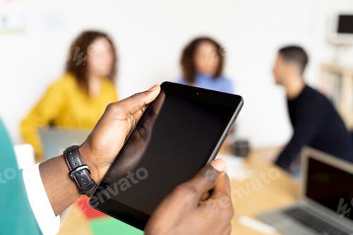 Preview: Close-up of businessman in office using tablet with colleagues in background