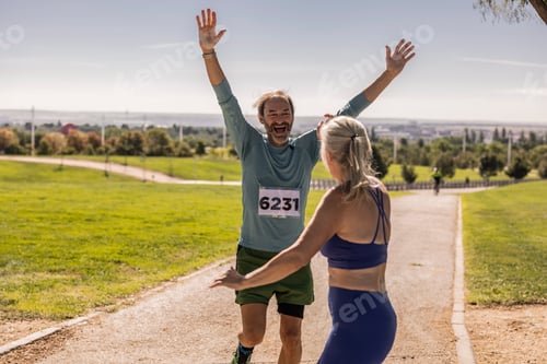 Preview: Senior man winning marathon, raising arms in victory, woman congratulating him