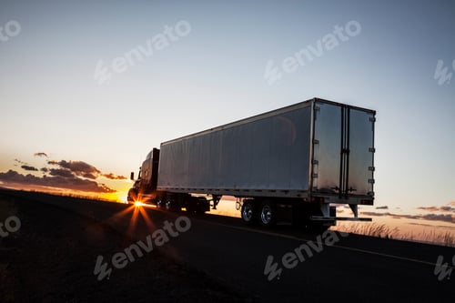 Preview: Silhouette of a commercial truck driving on a highway at sunset.
