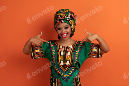 Preview: Cheery black woman in african clothing pointing at herself