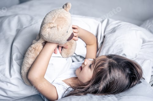 Preview: Little cute girl in bed with a teddy bear early in the morning.